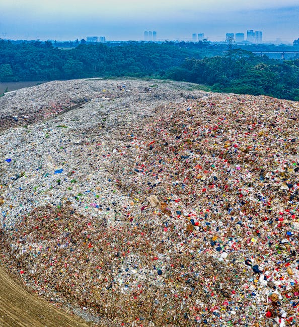 A large outdoor pile of mixed scrap metal and discarded household appliances, including broken chairs, metallic frames, and electronic waste, stacked and scattered across a gravel surface under a clea