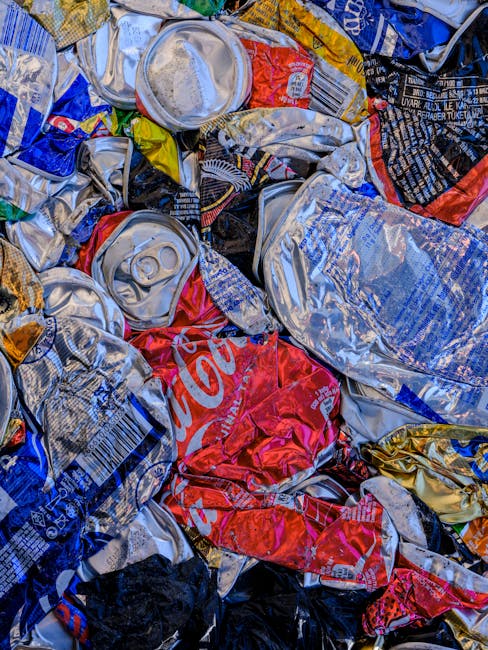 A black, cylindrical public trash bin with a domed lid is positioned on a cobblestone street. The bin is overflowing with various waste items, including crumpled paper and plastic packaging, with some